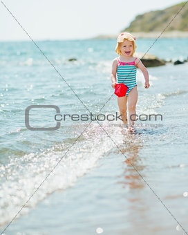 Happy baby with pail running along seashore