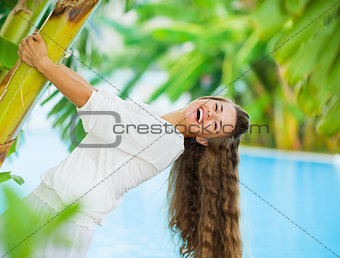 Laughing young woman leaning on tropical palm
