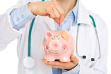 Closeup on medical doctor putting pill into piggy bank