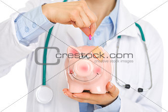 Closeup on medical doctor putting pill into piggy bank
