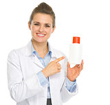 Smiling cosmetologist pointing on bottle of sunscreen