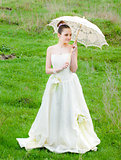 Beautiful bride with lace umbrella on green grass
