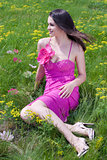 Young woman in pink dress sitting on green grass