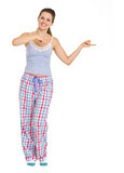 Full length portrait of young woman in pajamas pointing on copy 