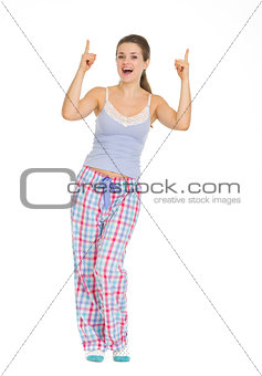 Full length portrait of young woman in pajamas pointing up on co