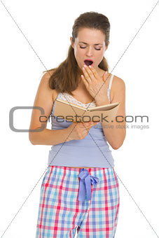 Young woman reading book before sleep and yawing