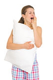 Happy young woman in pajamas with pillow yawing