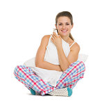 Smiling young woman in pajamas sitting with pillow