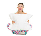 Happy young woman in pajamas sitting with pillow