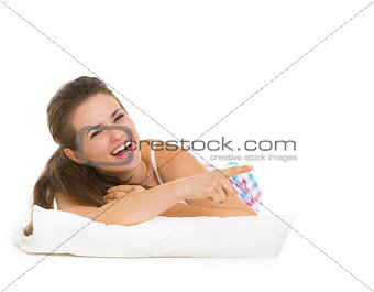 Happy young woman in pajamas laying on pillow and pointing on co