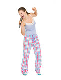 Full length portrait of young woman in pajamas singing in microp