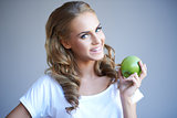 Head shot of woman holding green apple against grey