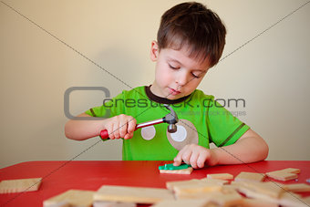 Cute boy working with hammer and nail at construction project