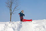 Boy pulling red plastic sledge to a snowy hill