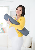 Asian pregnant woman holding yoga mat