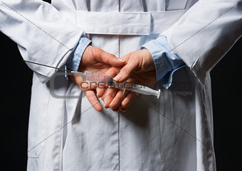 Closeup on medical doctor woman hiding syringe behind back