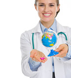 Closeup on smiling medical doctor woman holding pills and globe