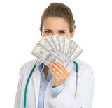 Medical doctor woman hiding behind fan of dollars