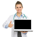 Smiling medical doctor woman showing laptop and thumbs up