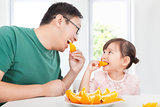 happy little girl with father eating orange