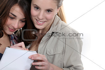 Two teenage girls writing on note pad