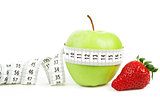 Measuring tape wrapped around a green apple and strawberry as a symbol of diet