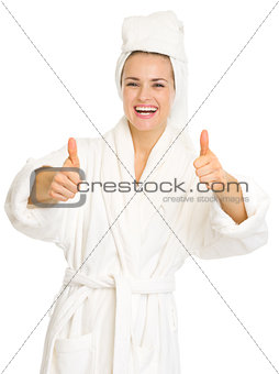 Smiling young woman in bathrobe showing thumbs up