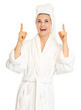 Happy young woman in bathrobe pointing up on copy space