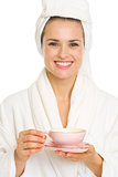 Happy young woman in bathrobe holding cup of tea