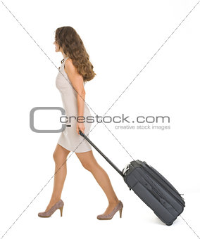 Young woman walking with wheels suitcase. Side view