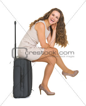 Smiling young woman sitting on wheels suitcase