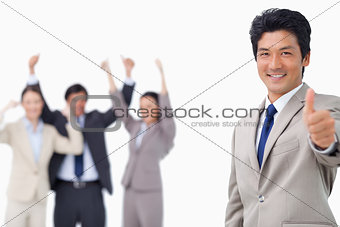 Businessman giving thumb up while getting celebrated