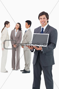 Smiling salesman showing laptop screen with team behind him