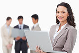 Smiling saleswoman with laptop and colleagues behind her