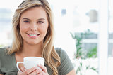 Woman holding a mug in her hands and smiling, while looking forw