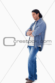 Man crossing his arms looking down and leaning against a wall