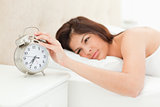 A woman lying in her bed with her hand on the alarm clock, which
