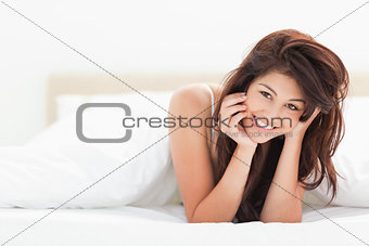 Woman is lying at the end of the bed under the quilt while smili