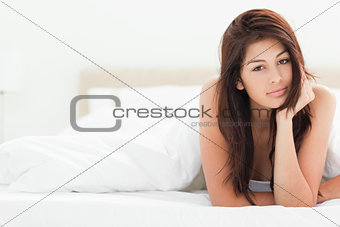 A woman lying at the end of the bed under the quilt with one arm