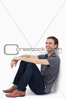 A dark brown hair man smiling while sitting against a wall 
