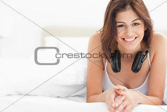 Woman on the bed with headphones around her neck, smiling and lo
