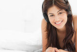 Woman smiling with earphones on her head, while lying with a qui