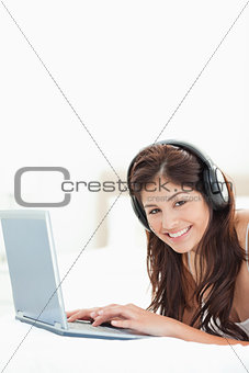 Close up, woman with headphones and a laptop lying on a bed