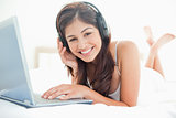 Woman looking ahead smiling, while using a laptop and headphones
