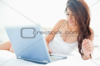 Woman lying upward across the bed while using her laptop