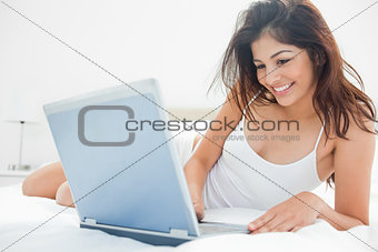 Woman lying across her bed, using her laptop and enjoying what s