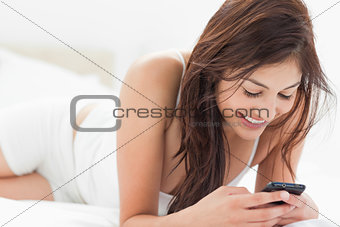 Woman smiles as she uses her phone while relaxing on her bed