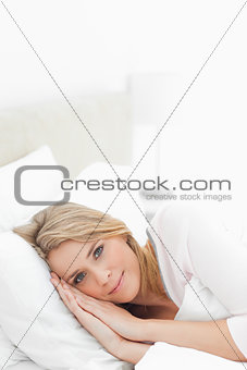 Woman resting in bed, eyes open and hands placed beside her head