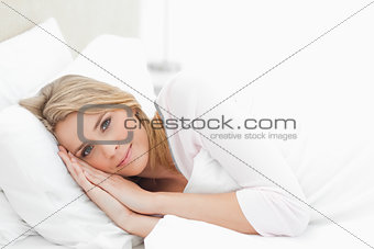 Horizontal shot, woman resting in bed, eyes open with hands and 
