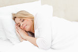 Woman sleeping in bed with hands placed beside her head on the p